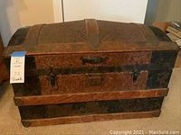 Front view of antique trunk showing embossed metal coverings with original hardware, wood framing, latch lock, and broken off handle attachments.