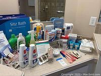 Assorted bathroom products arrayed on a bathroom counter including Sitz Bath box, bottles of Ammens powder, sprays, bandages, and medical supplies.