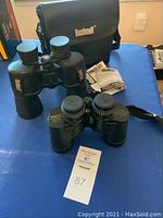 Two sets of binoculars displayed on a table with carrying cases and manuals visible, Bushnell logo on one case and binoculars.