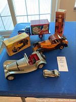 Photo shows two metal and wood roadster models, vintage Pepsi delivery truck in original box, and Avon after shave collectible on blue tablecloth.