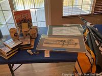 View of entire lot on table including framed sketches, mugs, DVD set, Wheaties box in plastic case, watch, pins and Steelers flag.