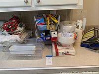 Overview of assorted kitchen paper products, cups, plates, napkins, towels, and storage bins on countertop.