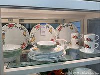 Photo showing stacked plates, bowls, cups, and saucers with fruit pattern and green rim