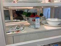 Ceramic fruit-themed serving pieces including a colander, cream and sugar set, and trays.