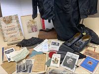 Wide shot of collection showing black dress jacket, shoes, hat, fan, purse, documents, and framed needlepoint sampler.
