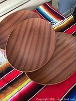 Four teak wood plates stacked on a colorful striped fabric, showing shape and wood grain.