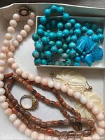 Overview of all items laid in box: three bead necklaces, ring, pair of earrings