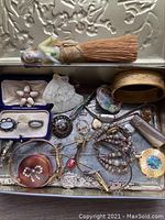 Metal tin tray filled with assorted vintage jewelry pieces and porcelain figurines