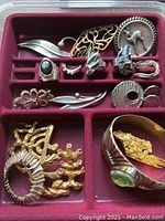 Red velvet tray displaying a variety of vintage mid-century silver and mixed-metal jewelry pieces arranged in compartments.