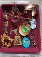 Overview of mid-century costume jewelry pieces laid out in a red tray including brooches, cuff bracelets, earrings, and pendants.