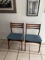 Front view of both teak ladder back chairs against a white textured wall
