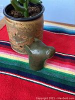 Front and side view of the Inuit soapstone dog head sculpture next to a decorative ceramic pot on a colorful striped fabric.