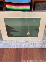 Framed serigraph print showing a sailboat on water with rocky coastline and moon, with visible framing and mat.