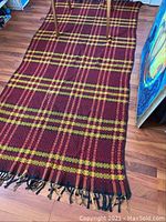 Full view of vintage 5x8 feet plaid rug or throw on hardwood floor showing red and yellow pattern and fringed edge.