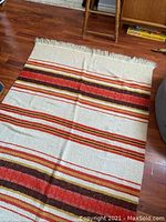 Full view of vintage rug laid out on hardwood floor showing striped pattern and fringes on ends