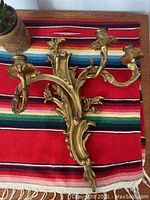 Vintage brass wall sconce resting on a colorful striped textile, showing the decorative leafy arms and three candle holders.