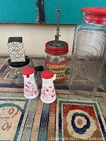 Photo showing full lot of vintage kitchen items including glass jars, a grater, and salt and pepper shakers on a patterned surface.