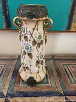 Front view of the antique Amphora vase showing the floral relief against crackle glaze glaze with gold handles and dark top band.