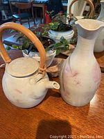 Photo of round vintage studio pottery teapot with bamboo handle beside tall vase on wooden table