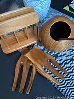Full view of the three teak kitchen items on a table: the nut bowl with spoon inside, napkin holder, and salad tongs