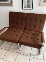 Front view of two-seat chrome tubular frame love seat with brown tufted cushions.