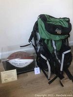 Both items displayed side by side on floor: signed football in case and backpack