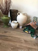 Four vases of varying sizes and one birdhouse with food packets displayed on wood flooring against wall.