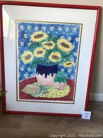 Framed watercolor artwork showing bright sunflowers in vase, red frame, and part of the floor