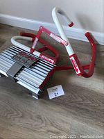 Emergency fire escape ladder folded on wood floor showing hooks and aluminum rungs
