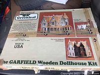 Box lid showing front image of the dollhouse and descriptive text including brand, style, and features of The Garfield dollhouse kit by Greenleaf.
