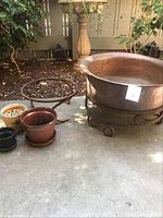 Wide shot showing the copper firepit with wrought iron stand, and three flower pots of different sizes arranged nearby on concrete