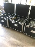 Three black rolling road cases opened showing DVDs inside