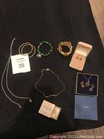 Full view of seven pieces of vintage costume jewelry including bracelets, necklaces, and earrings displayed on dark fabric.