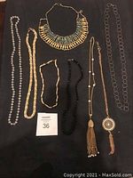 All 8 vintage necklaces laid out on black surface showing variety in style and materials including pearls, beads, metal chains and pendants.