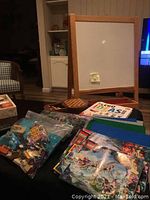 Overview photo showing a stand-up whiteboard, LEGO books, base plates, bags of LEGO pieces, and a wooden travel chess board on a table.