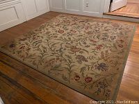 Full view of the wool pile rug on hardwood floor, showing floral tapestry design with colors red, green, purple, and brown on beige background.