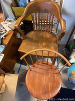 Two wooden chairs together, one large with armrests and slatted back, one smaller swivel chair with round seat and spindle back.