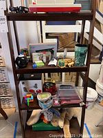 Shelf containing various small toys including a boxed table pool set, Rubik's cube, wooden puzzles, patches, pins, dice, and a plastic scenic cup.