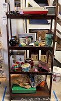 Full view of the tapered bookshelf showing three shelves with various items placed on them (not included in lot). Visible scratches on the wood surface.