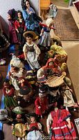 Overview of about 20 vintage dolls arranged on a surface showing a variety of traditional costumes and props.