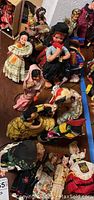 Photo showing a grouping of vintage collectible dolls dressed in international traditional costumes arranged on a wooden surface.