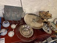 Table displaying four Waterford crystal champagne flutes, blue and white porcelain tea set with matching saucers, and various silver serving trays and bowls.