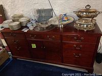 Wooden console with drawers and shelves visible, top of console surface showing scratches and marks. Various items placed on top, not included in lot.