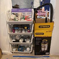 Photo showing Stanley Wet/Dry Vacuum retail box alongside a 4-bin plastic storage organizer containing multiple types of light bulbs.