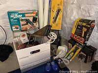 Complete lot of power tools and accessories displayed including boxed rotary tool, heat gun, tile cutter, radio, walkie talkies, wobble clock, and tire chains.