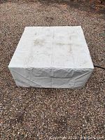 Fire pit unit covered with white protective cover placed outdoors on gravel
