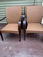 Photo showing two brown wicker patio chairs from the front, highlighting the woven synthetic material and wooden arms/legs.