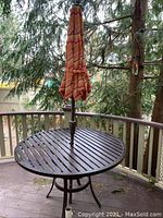 Top view of round metal outdoor table with umbrella inserted through center hole. Table surface shows scrape mark and dirt.