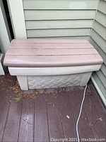Closed view of beige plastic outdoor storage box with textured sides and smooth lid on wooden deck corner.