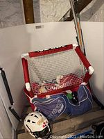 Full set of hockey equipment including pads, sticks, helmet, bag, and small practice net in basement corner.